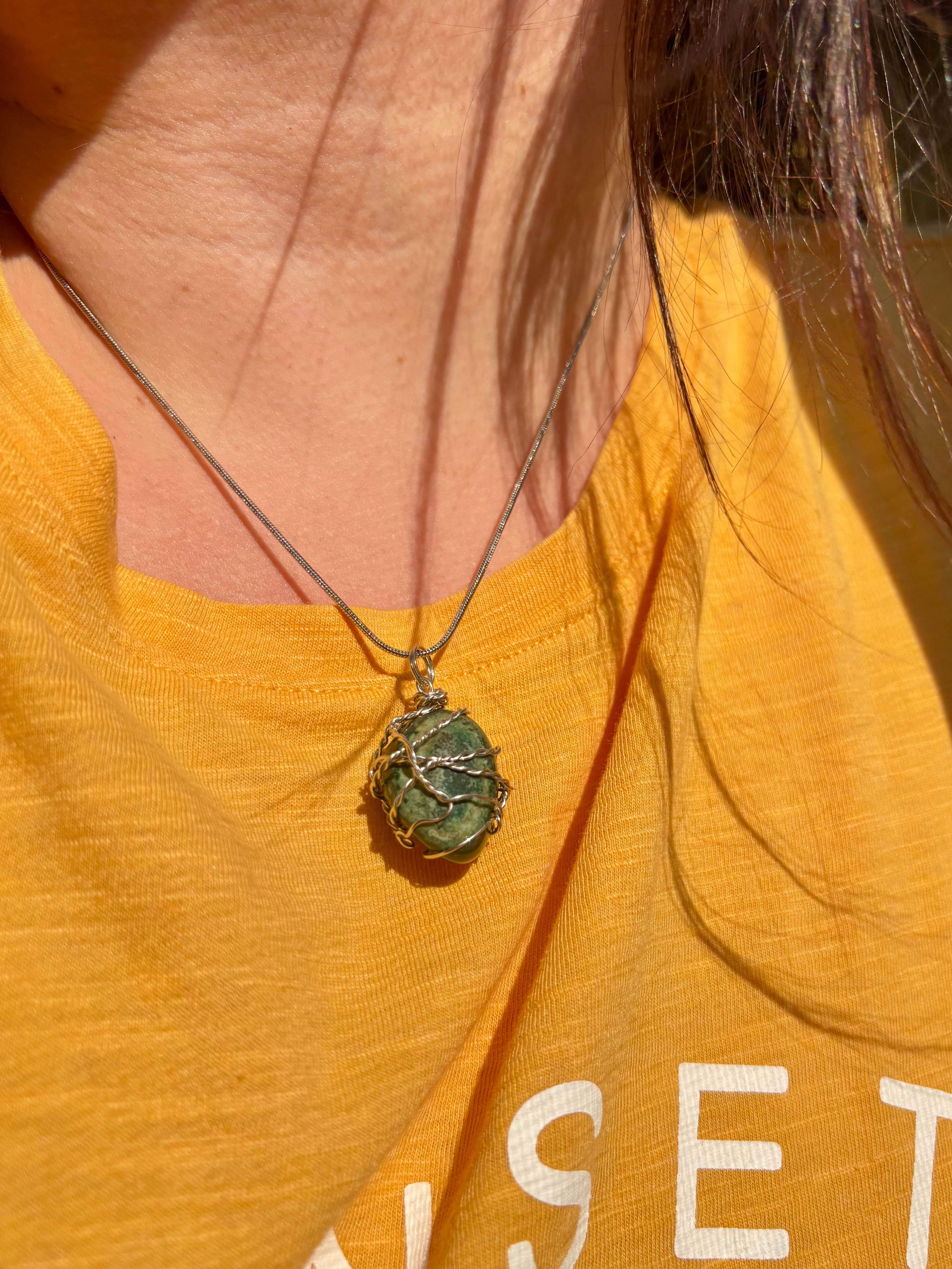 Person wearing a yellow shirt with a green pendant necklace.