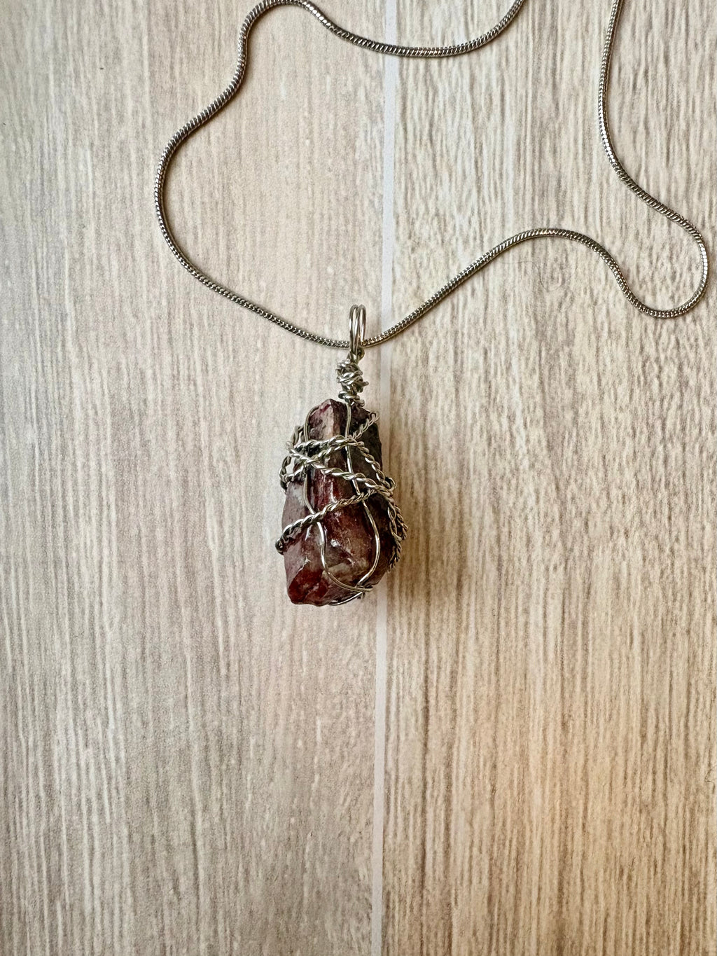 Necklace with a pendant featuring a rough maroon stone on a wooden surface