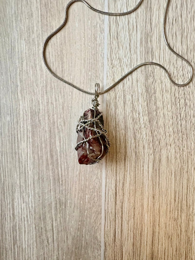 Necklace with a pendant featuring a rough maroon stone on a wooden surface