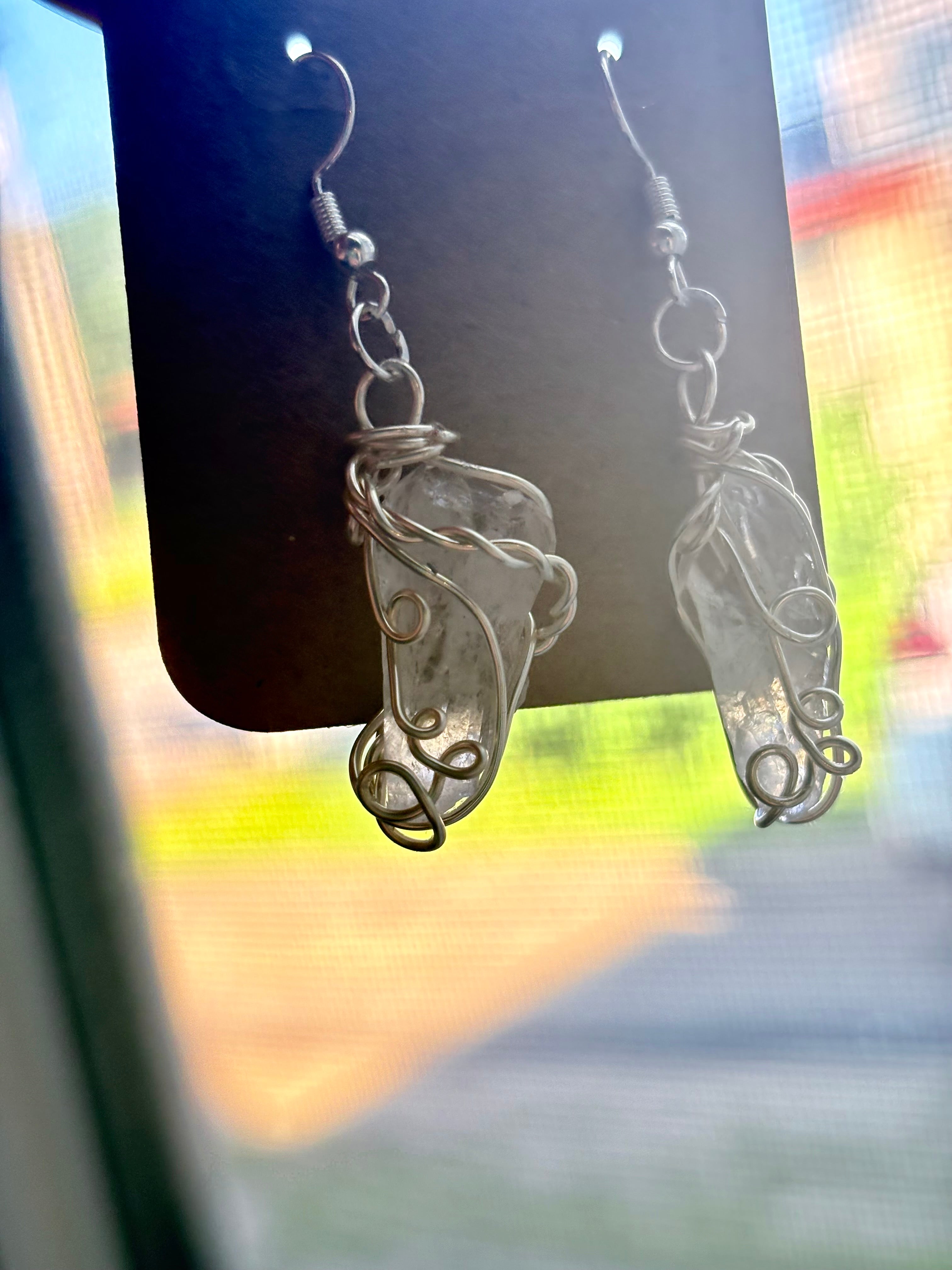 A pair of silver-toned dangling earrings with irregular clear crystal pieces wrapped in wire, hanging from a black display card. 