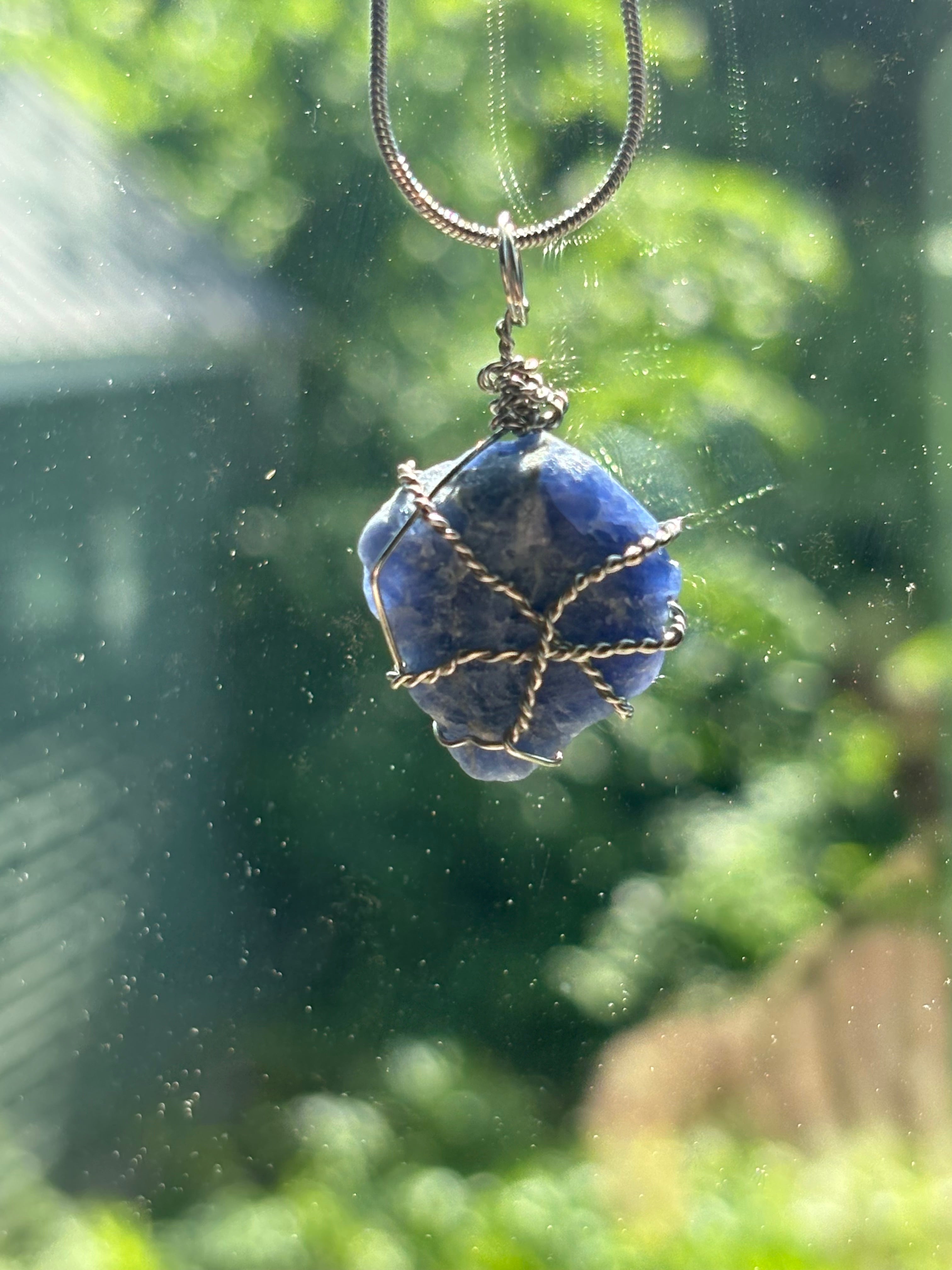 Blue stone pendant on a chain with a blurred green outdoor background