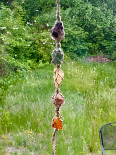 Decorative hanging with stones against a natural background of greenery. Includes purple amethyst, blue flourite.