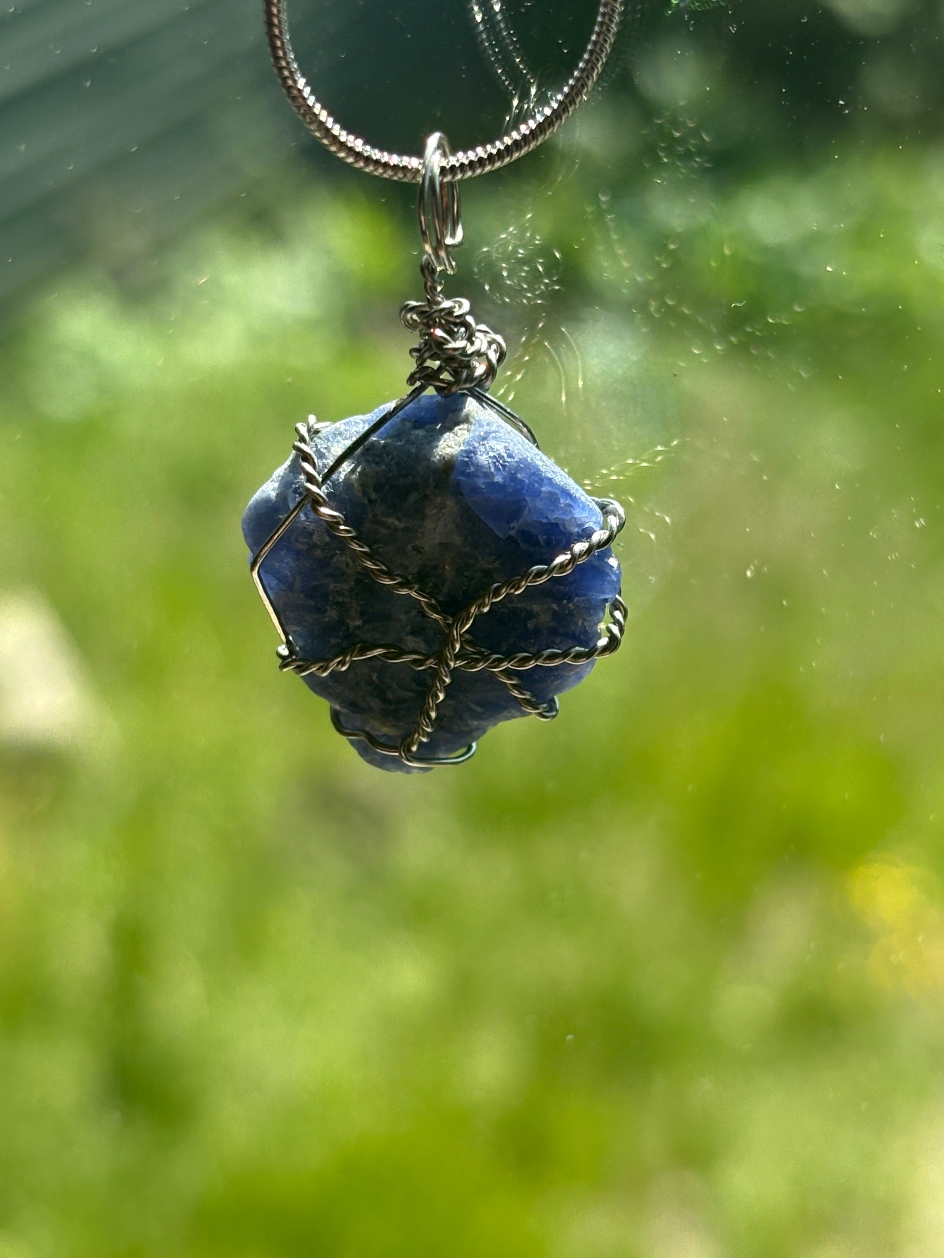 Blue stone pendant on a chain against a blurred green background